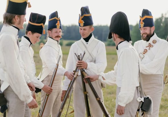 A group of historical reenactors in military uniforms stacking rifles outdoors in a field.