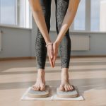 An adult woman performs yoga on a sadhu board indoors, focusing on balance and mindfulness.