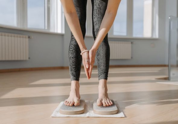 An adult woman performs yoga on a sadhu board indoors, focusing on balance and mindfulness.