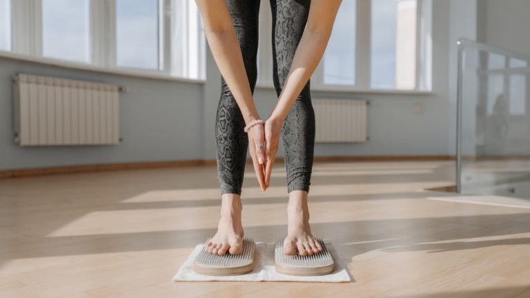 An adult woman performs yoga on a sadhu board indoors, focusing on balance and mindfulness.