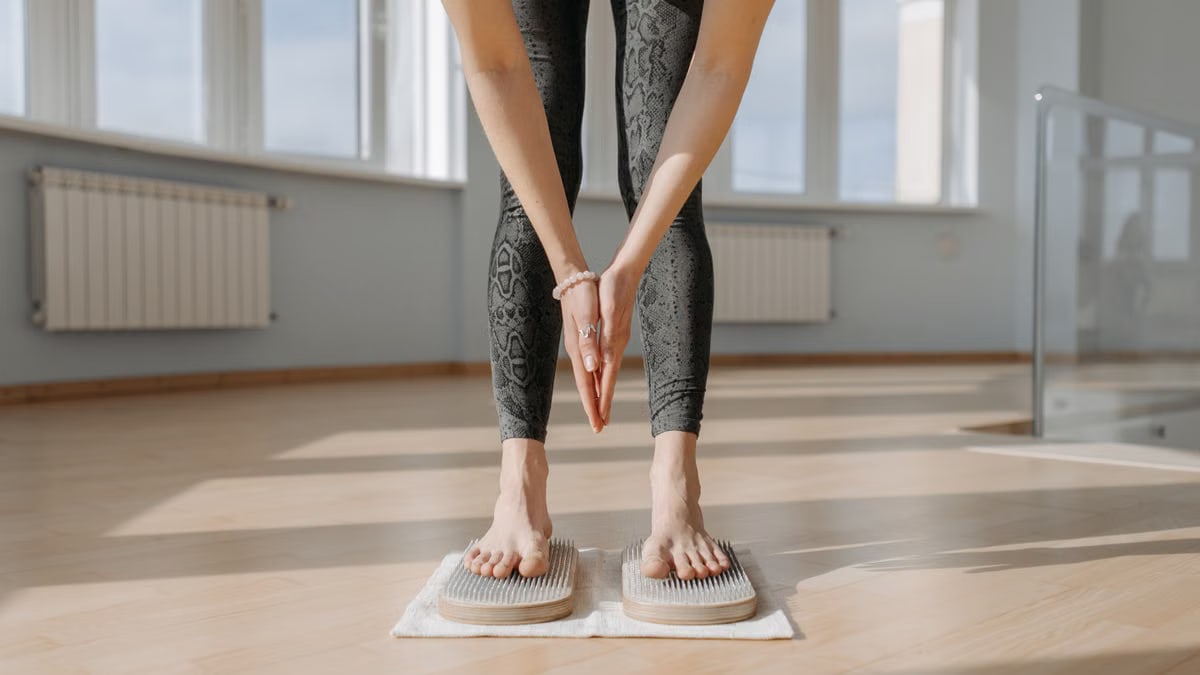 An adult woman performs yoga on a sadhu board indoors, focusing on balance and mindfulness.